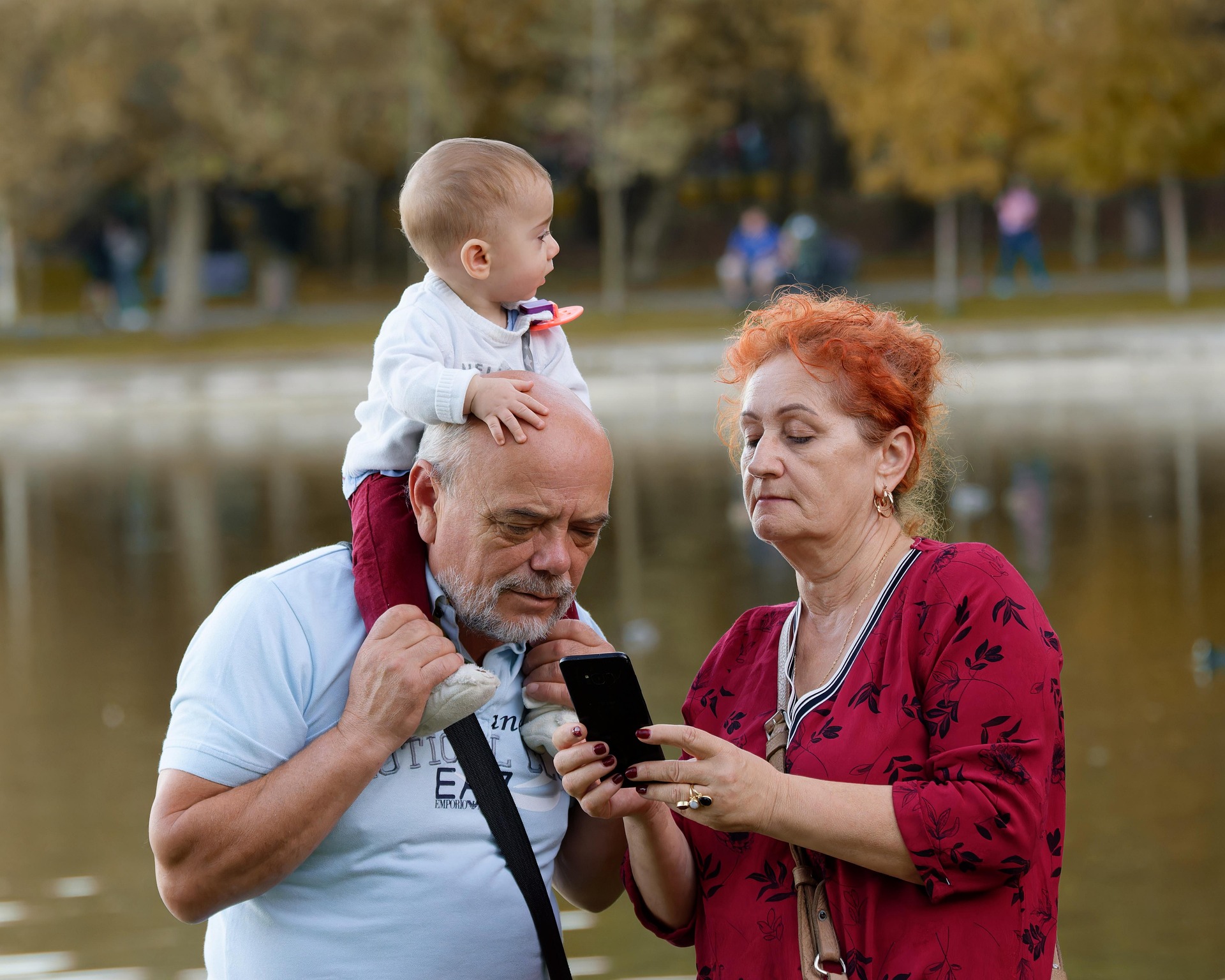 Na zdjęciu babcia i dziadek, przeglądający coś w smartfonie. Seniorzy opiekują się wnukiem.
