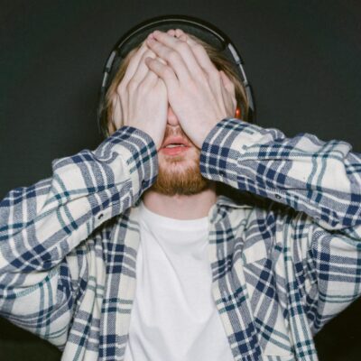 mężczyzna w słuchawkach nausznych z zakrytą dłońmi twarzą