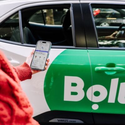 osoba trzyma smartfon w ręce stojąc przed taksówką z logo bolt