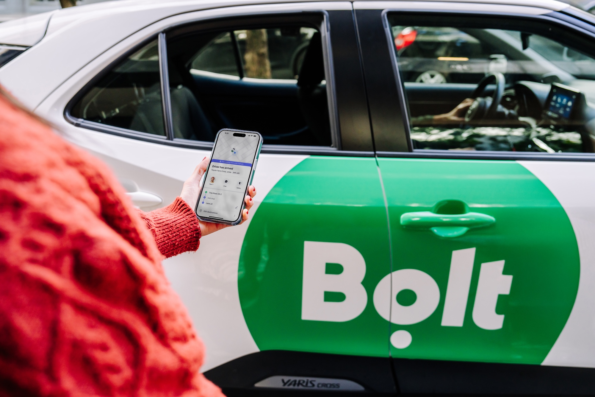 osoba trzyma smartfon w ręce stojąc przed taksówką z logo bolt