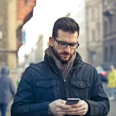 mężczyzna w czarnej kurtce ze smartfonem w ręce stojący przy ulicy