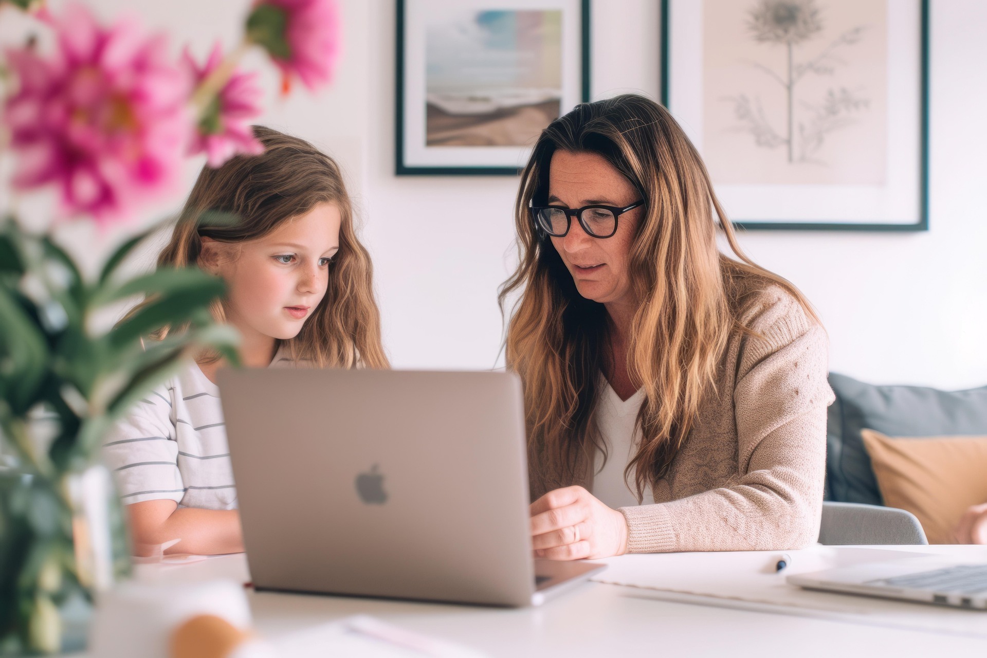 dorosła kobieta siedząca przy stole z kilkuletnią dziewczynką przed laptopem z logo firmy Apple