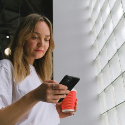 młoda dziewczyna z telefonem i kubkiem w rękach