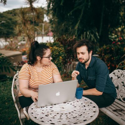 kobieta i mężczyzna siedzący przed laptopem na stoliku w ogrodzie