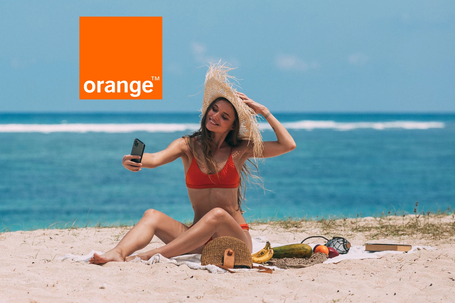 dziewczyna na plaży ze smartfonem w ręce, obok logo orange