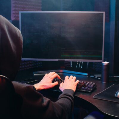 haker hacker siedzący przed komputerem w bluzie z kapturem na głowie
